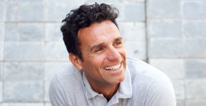 Smiling middle-aged man with curly hair wearing gray polo shirt