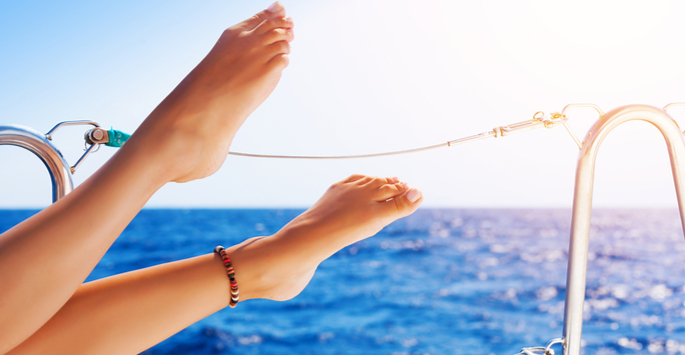 Woman's feet with anklet lifted on air while on a cruise with the blue ocean in the background