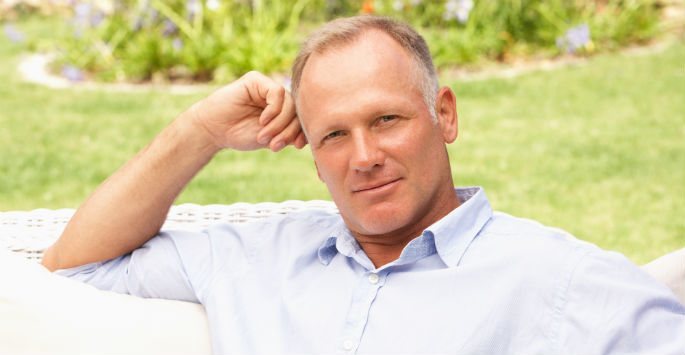 Mature man's portrait sitting in garden's white couch