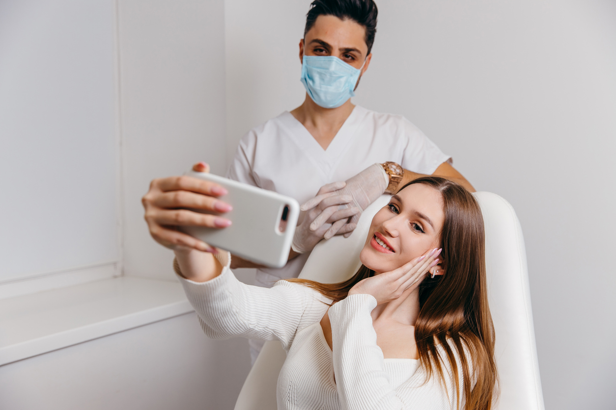 Happy brunette woman at beauty medical clinic. She is talking with doctor about face esthetics treatment. High quality photo