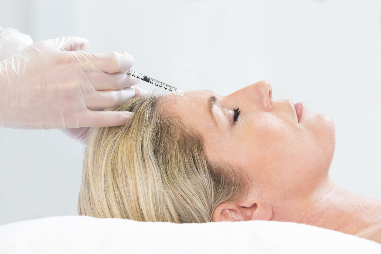 Woman lying down receiving botox injection in her forehead.