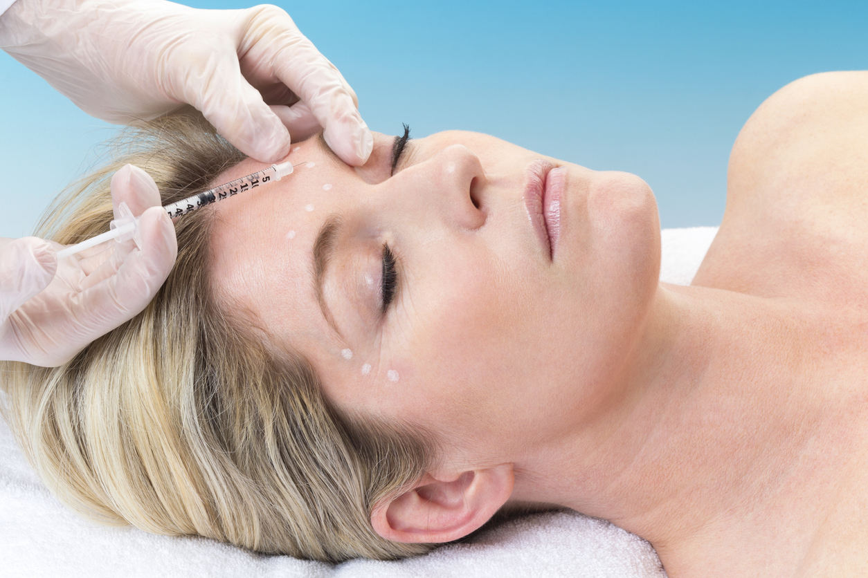 Woman lying down receiving botox injection in her forehead.