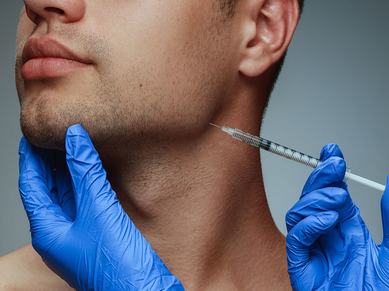 Close-up portrait of young man isolated on grey studio background. Filling botox surgery procedure.